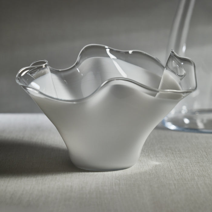 White glass wave-edge bowl with clear wavy rim, set on a neutral fabric surface.