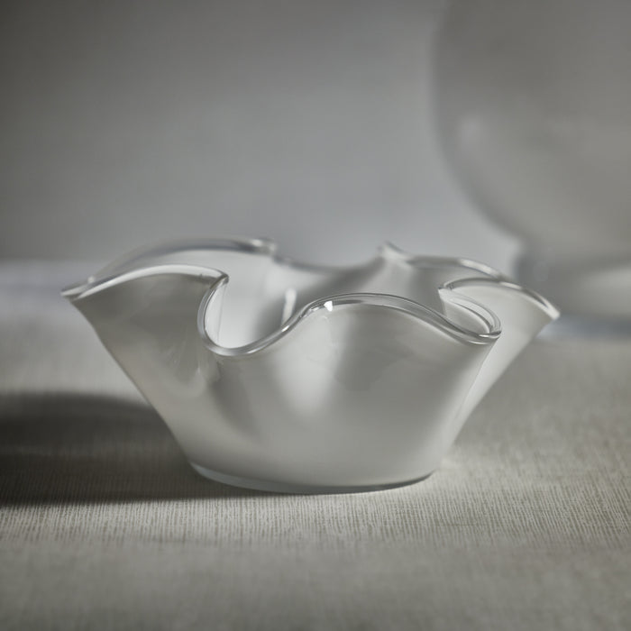 A white, wave-shaped glass bowl on a textured surface, with a blurred background.