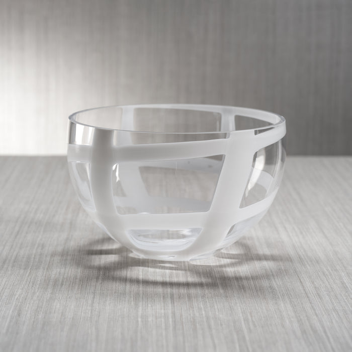 A clear glass bowl with white swirl stripes on a textured surface.