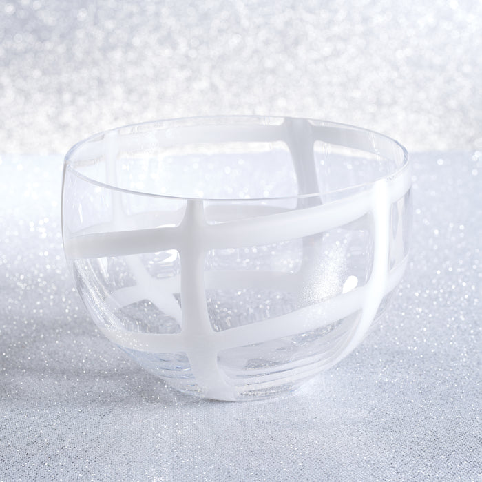 Clear glass bowl with white crossbar lattice, shallow rounded shape, sits on glittery silver surface.