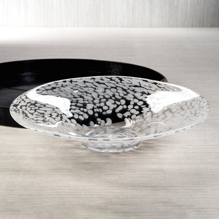 A clear glass centerpiece bowl with white confetti speckles displayed on a wooden surface.