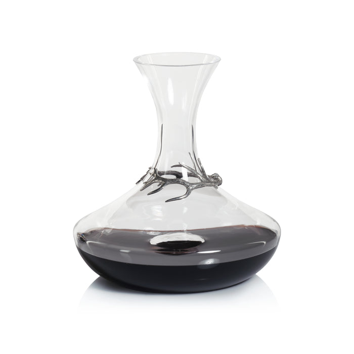 A clear glass wine decanter with a pewter antler accent on the top part.