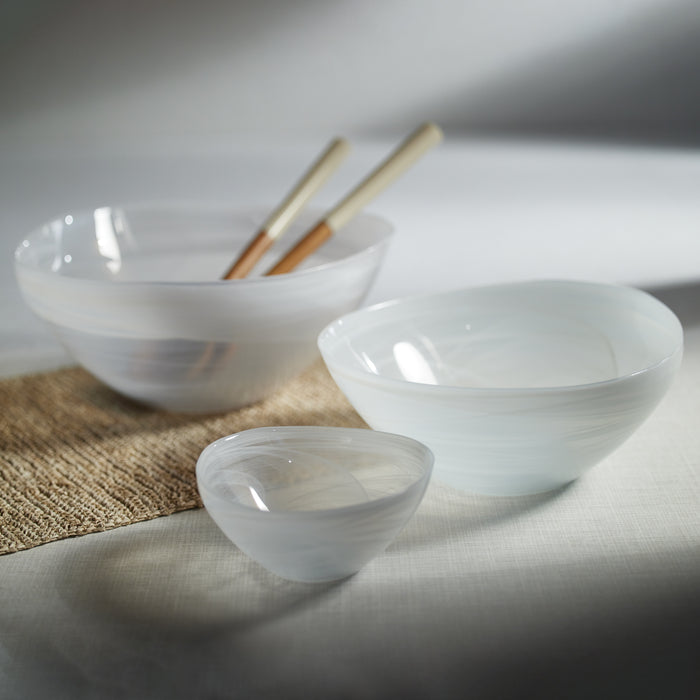 Set of six white alabaster glass bowls with subtle swirls, varying sizes, placed on a light surface with braided mat