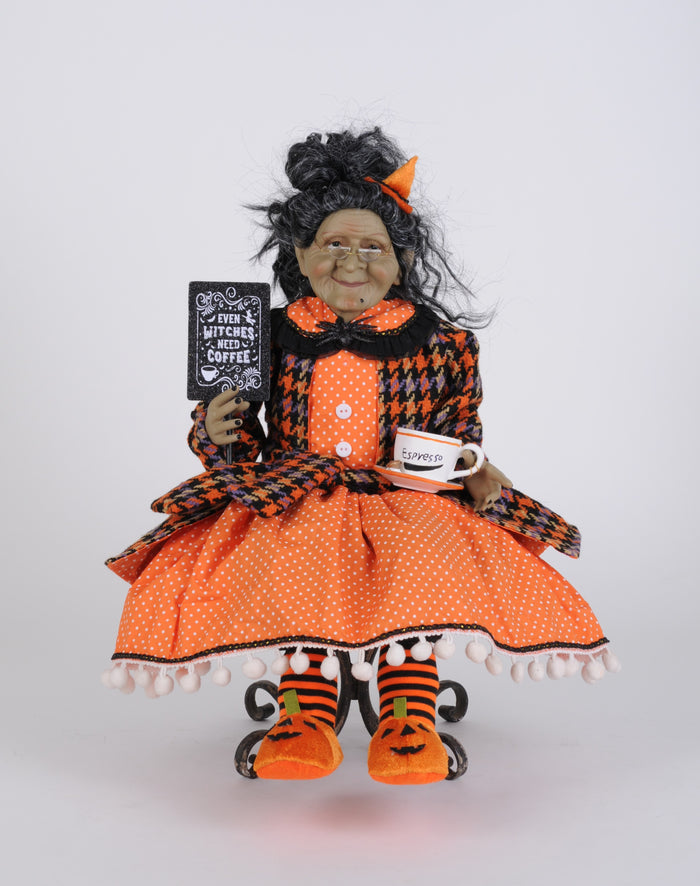 Halloween-themed doll in an orange and black outfit holding a sign and mug.