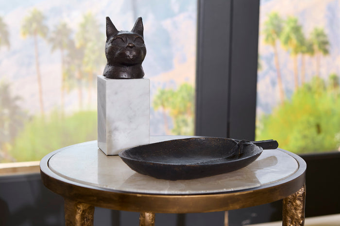 Decorative black cat sculpture on a marble pedestal with a black bowl on a round table.