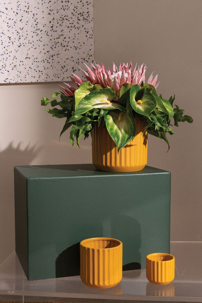 Yellow vase with pink flowers on a green surface against a speckled wall.