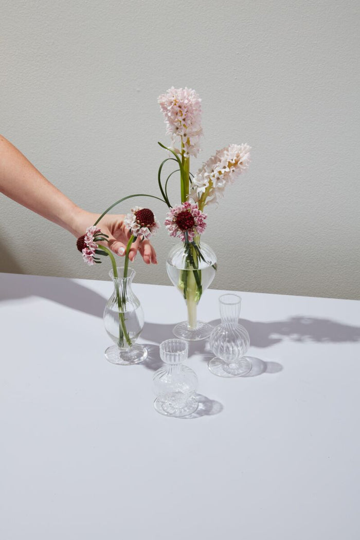 Hand arranging flowers in small glass vases on a light surface with a neutral background