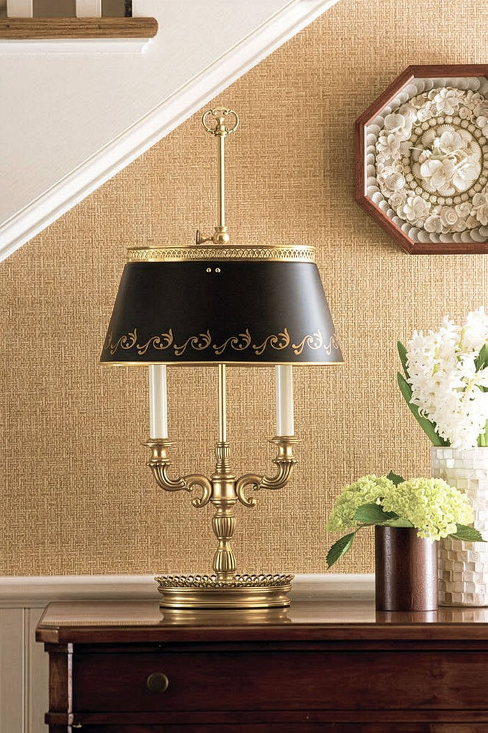 Decorative table lamp with black shade on a wooden surface against a textured wall.