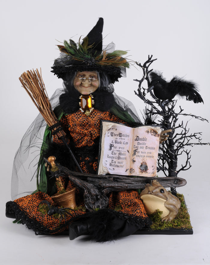 Halloween-themed figurine of a witch with broom, book, and crows on a white background