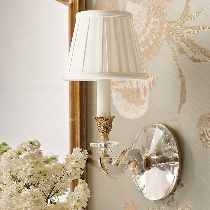 Wall sconce with crystal detailing and white floral arrangement on a decorative wall.