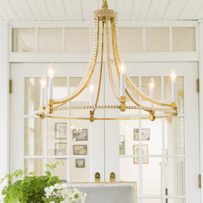 Gold chandelier with white candles in a room with white walls and framed pictures.