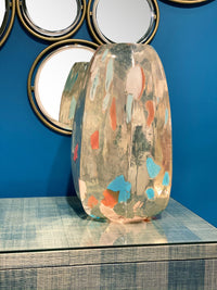 Decorative glass vase with colorful abstract design on a reflective surface with blue wall background