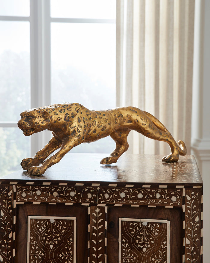 Gold panther figurine on a decorative wooden cabinet with white curtains in the background