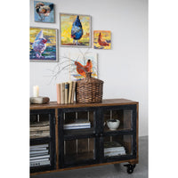 Wooden sideboard with decorative items and framed paintings of chickens on a wall.