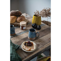 Table setting with bread, jam, and a mug on a wooden surface.