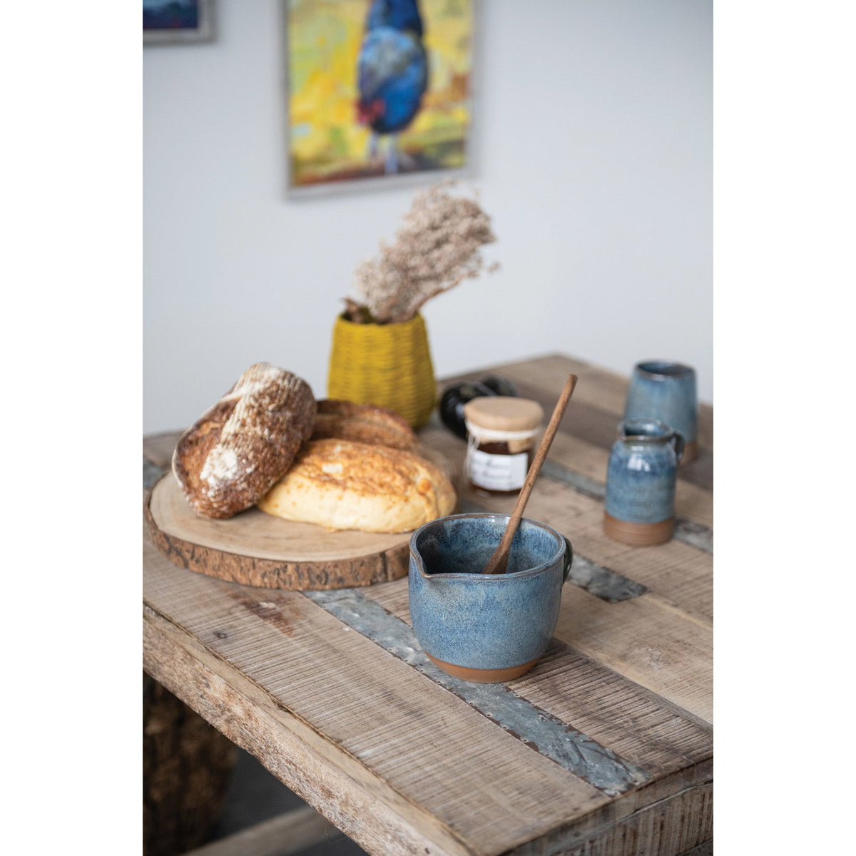 Bread on a wooden board with a blue ceramic bowl and spoon on a rustic wooden table.