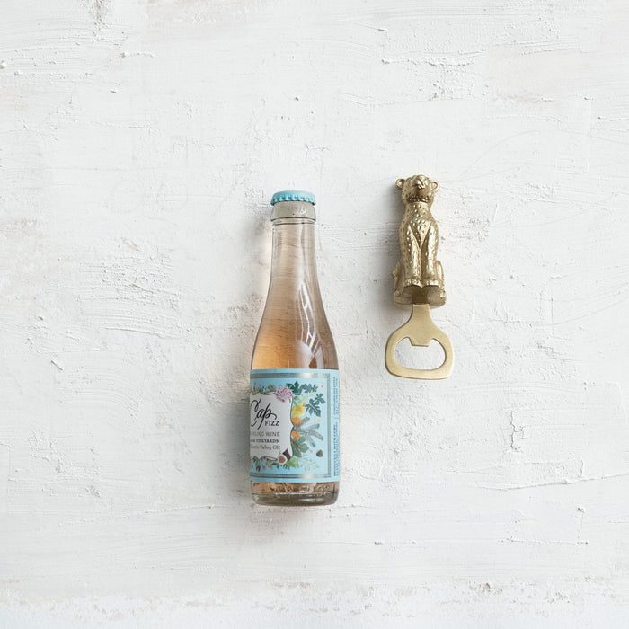 Leopard-shaped stainless steel bottle opener beside a small pink wine bottle with turquoise label on a white textured
