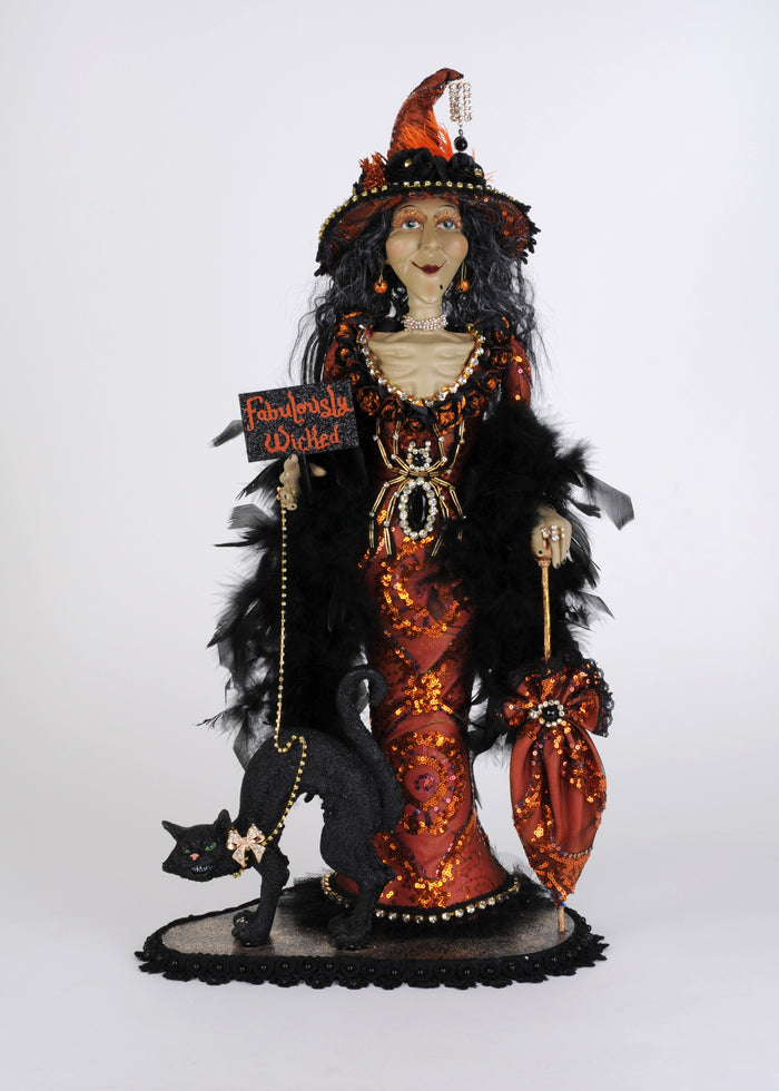 Halloween-themed doll with black cat, orange and black outfit, and feathered headdress on a white background.