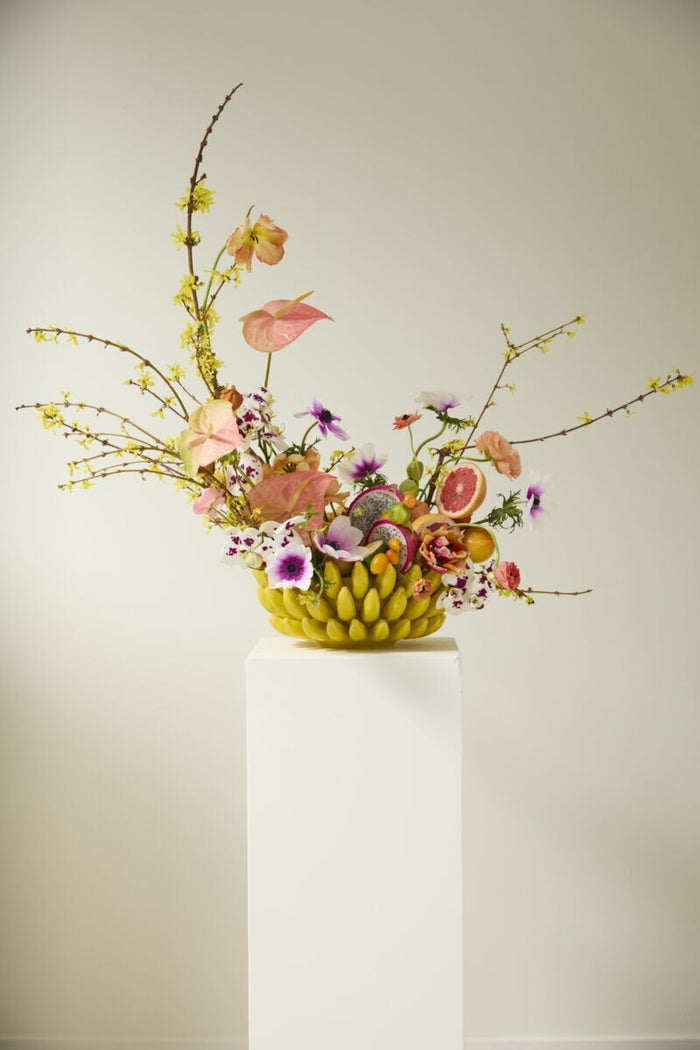 Floral arrangement in a yellow basket on a white pedestal against a beige background