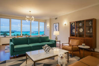 Marble-patterned conch shell on top of a marble coffee table inside of a Coco Plum living room with a mid-century modern wood china cabinet, teal green sofa, tan leather accent chair and geometric area rug.