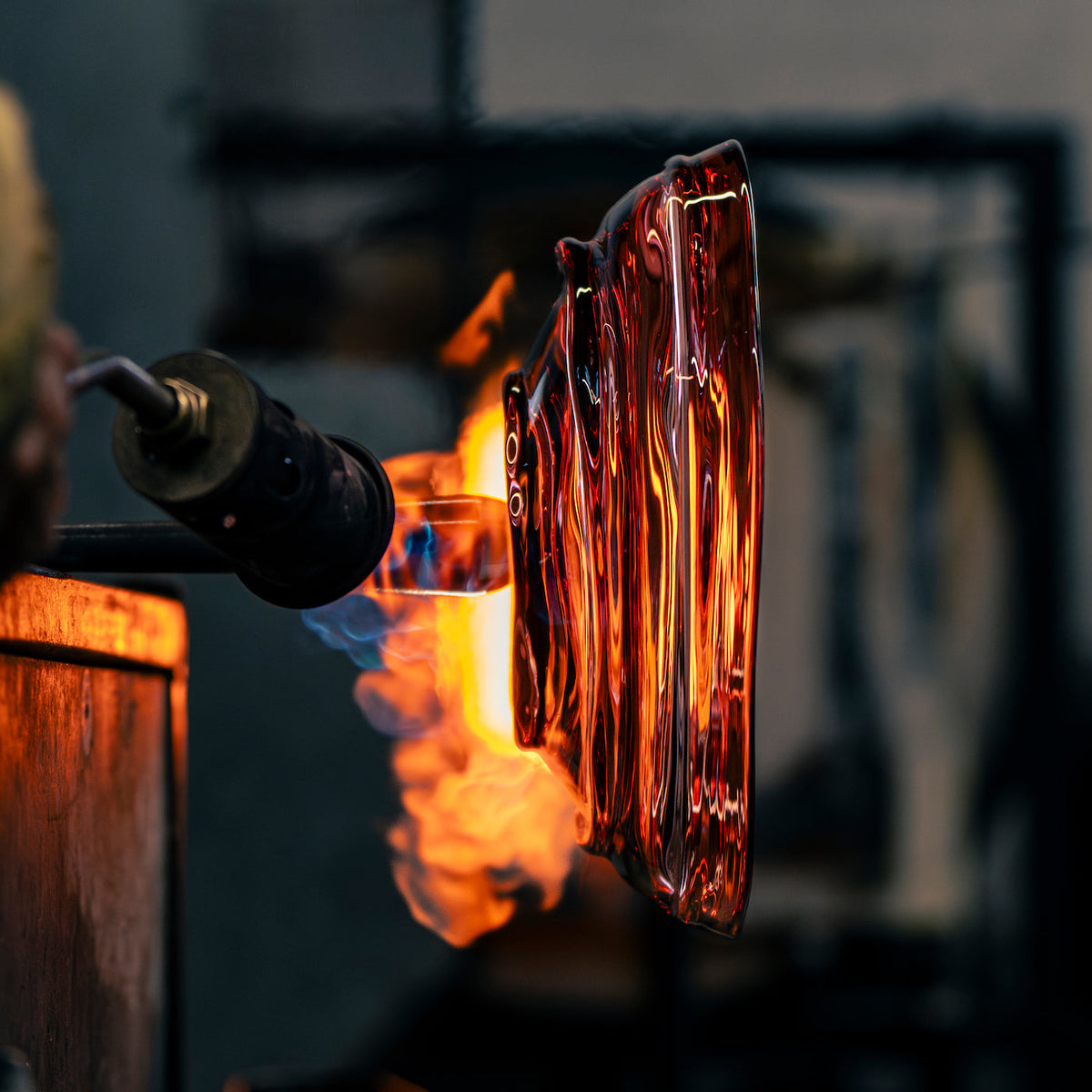 Glassblowing process with molten glass being shaped over a flame.
