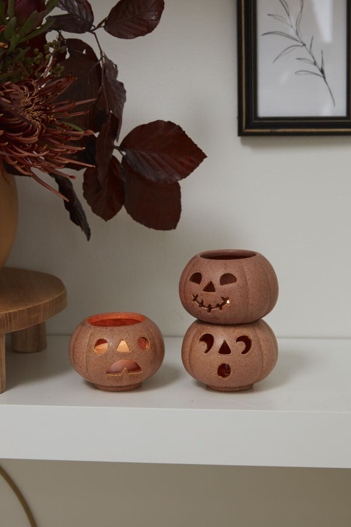 Three small ceramic pots on a white surface with a plant in the background