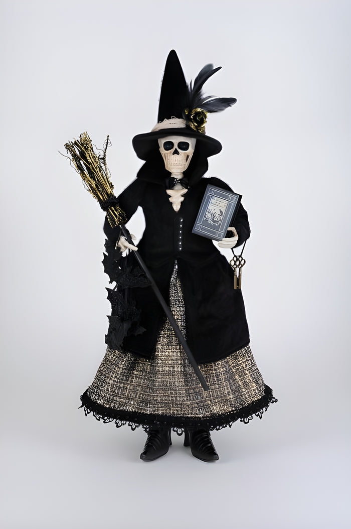Skeleton figure in a witch costume with broom and book on a white background