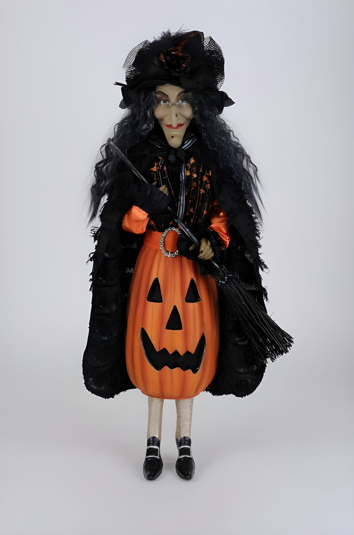 Halloween-themed doll with black cloak, pumpkin dress, and broom on a white background