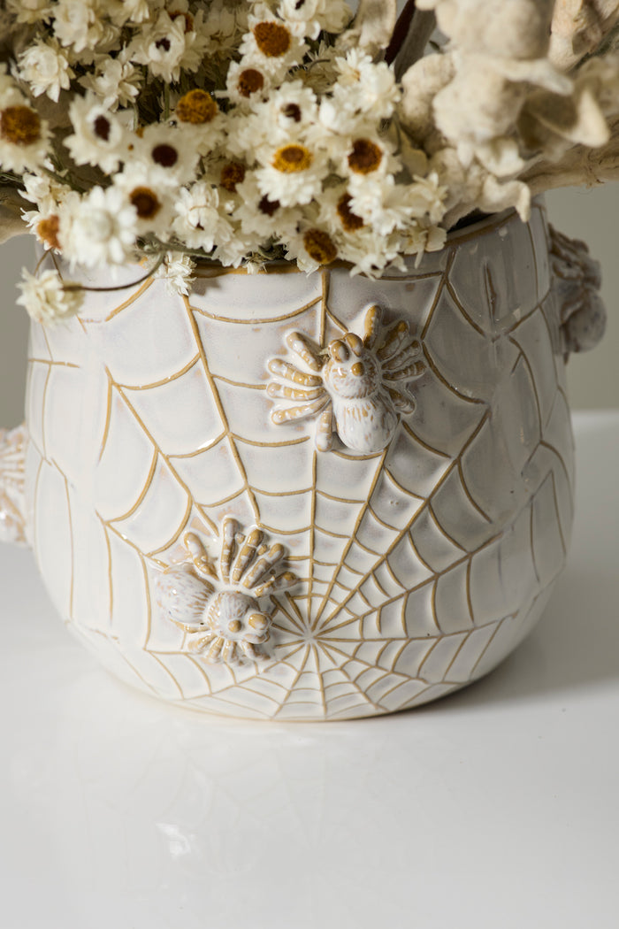 Decorative ceramic pot with spiderweb design and spider figures, containing dried flowers.