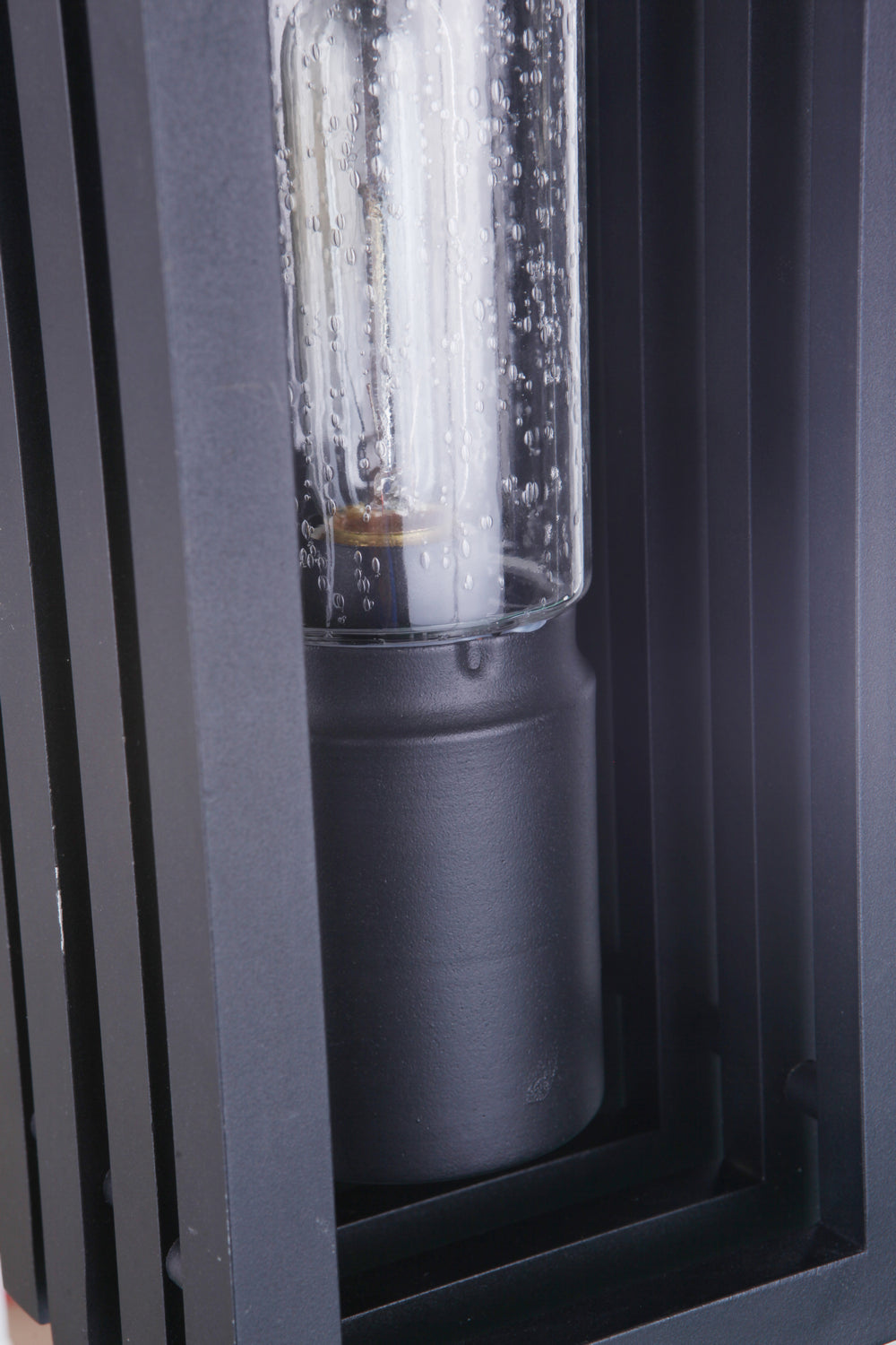 Carmel outdoor wall lantern in textured black with a clear glass tube and visible inner bulb, set within a dark metal frame.
