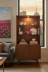 magenta Murano glass bowl inside of a mid-century modern china cabinet inside of a NYC luxury condo. The scene is a living room with a grey sofa and a wood coffee table.