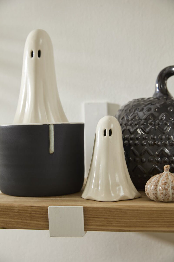 Two ghost-shaped decorative items on a shelf with a neutral background