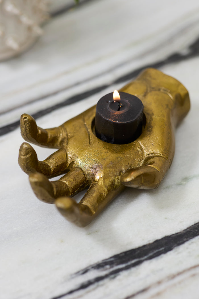 Bronze hand-shaped candle holder with a lit candle on a marble surface