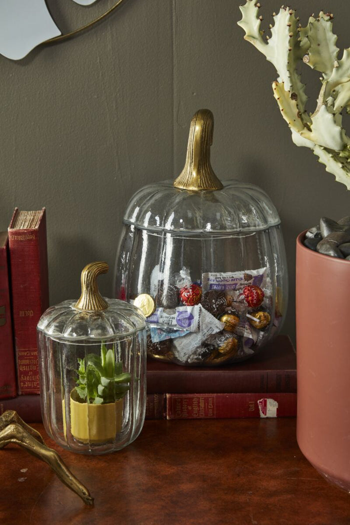 Decorative glass pumpkins with gold stems on a wooden surface with books and a plant.