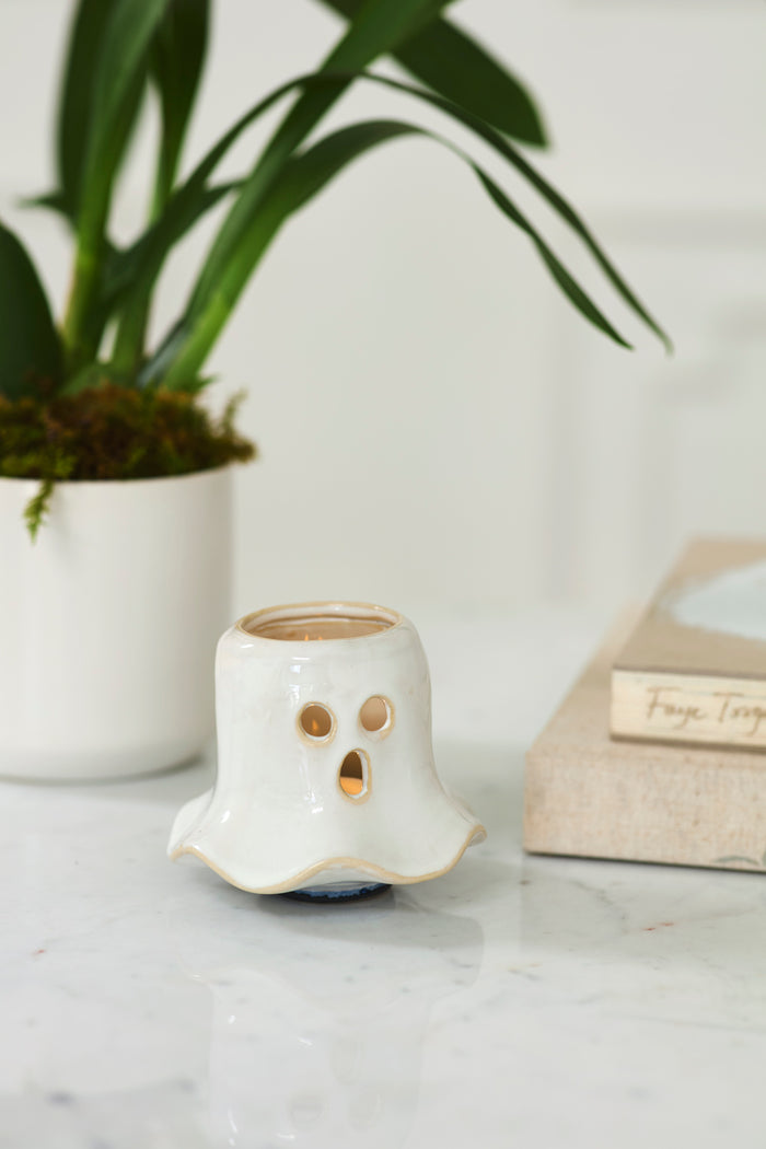 White ghost-shaped candle holder on a marble surface with a plant in the background
