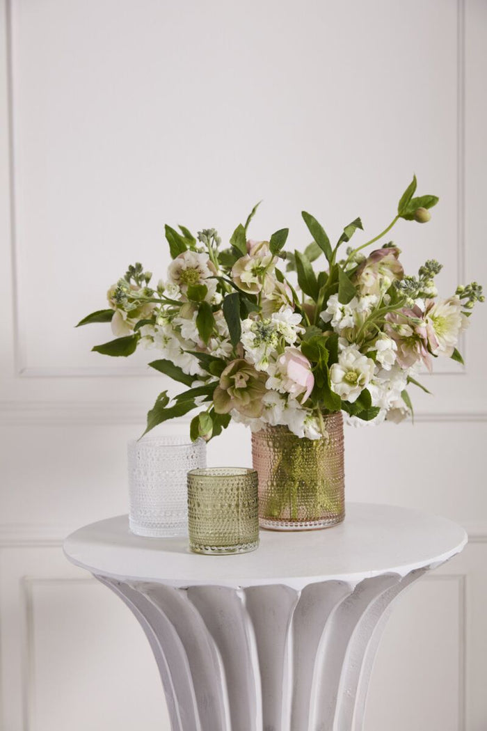 Floral arrangement in a vase on a white pedestal table against a white paneled wall.