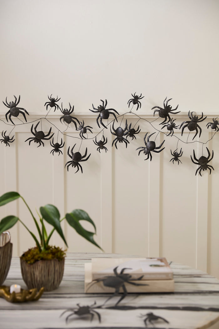 Halloween spider decoration on a wall with books and plants below.