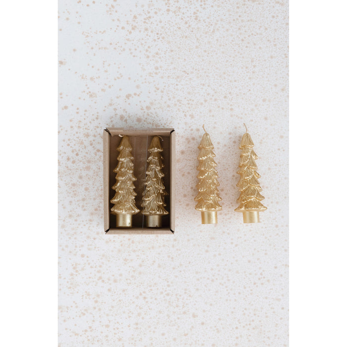 Two gold scented-free tree-shaped taper candles in a small brown box, plus two loose gold tree candles on a speckled beige