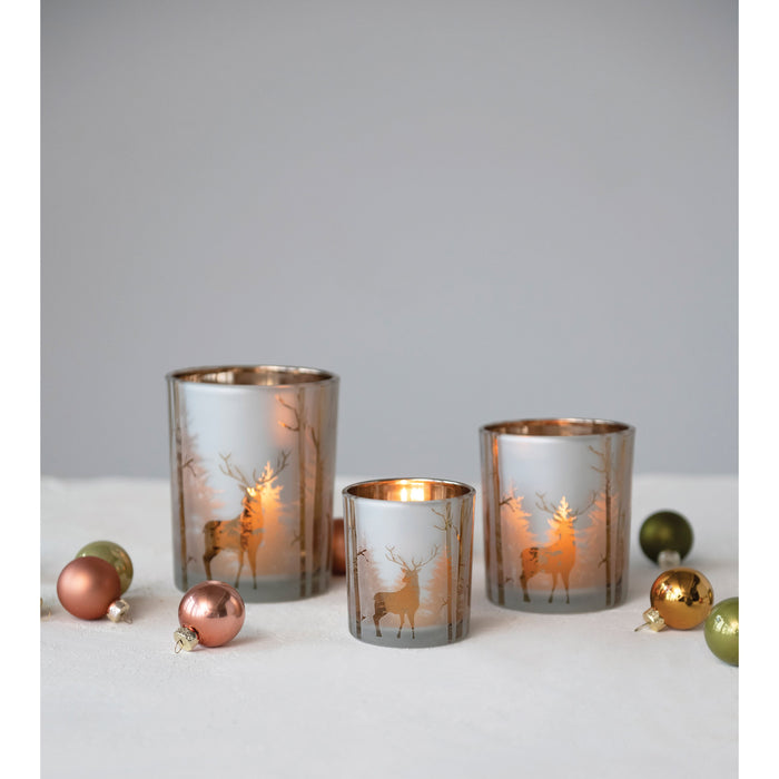 Mercury glass candle holders with copper interior and laser-etched reindeer forest silhouettes, set on a white surface with