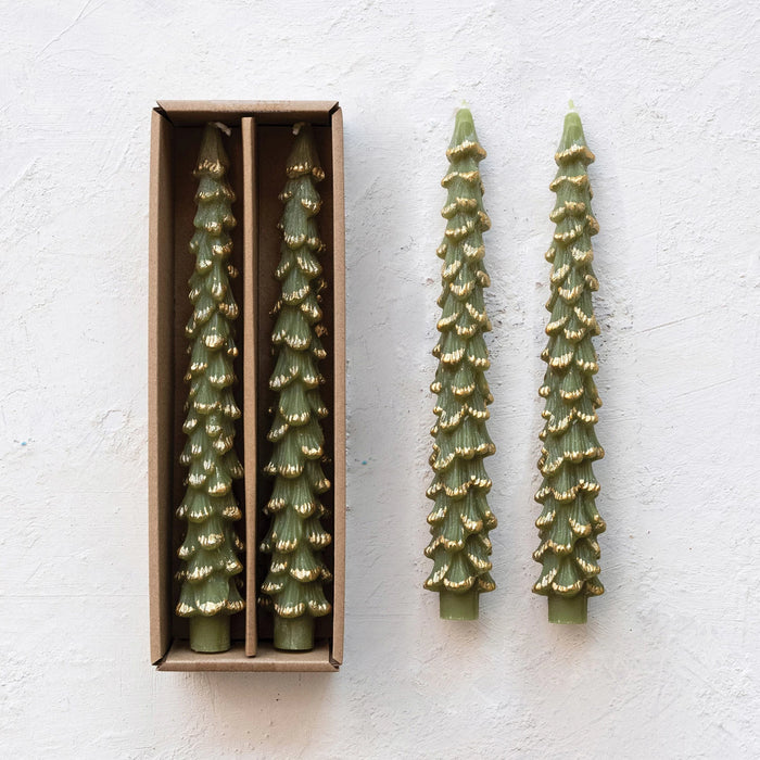 Set of two green tree-shaped taper candles with gold tips, in a brown cardboard box and loose beside it on a light textured