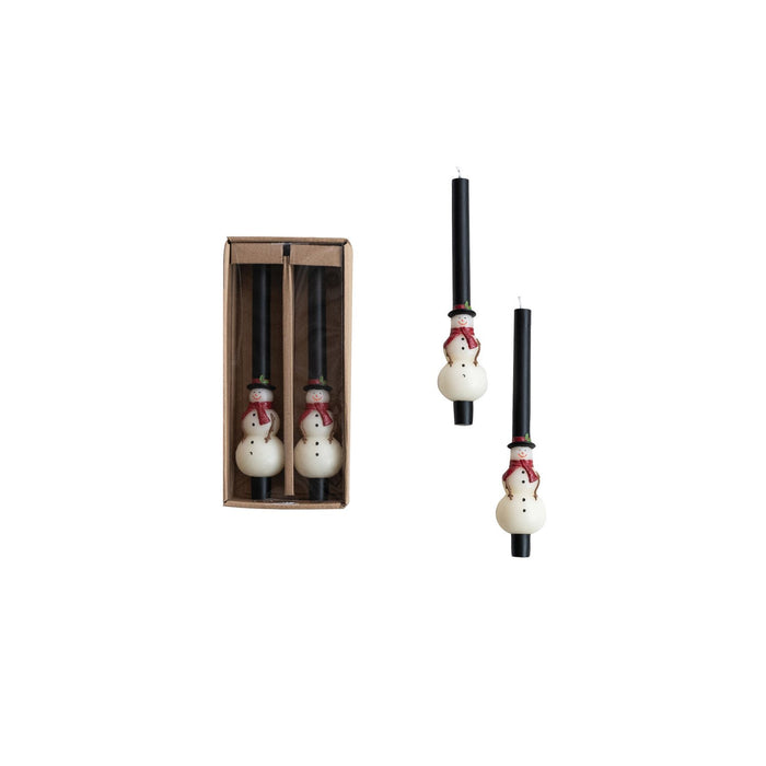 A set of two snowman-shaped taper candles with white figures and red details, presented in a brown box.